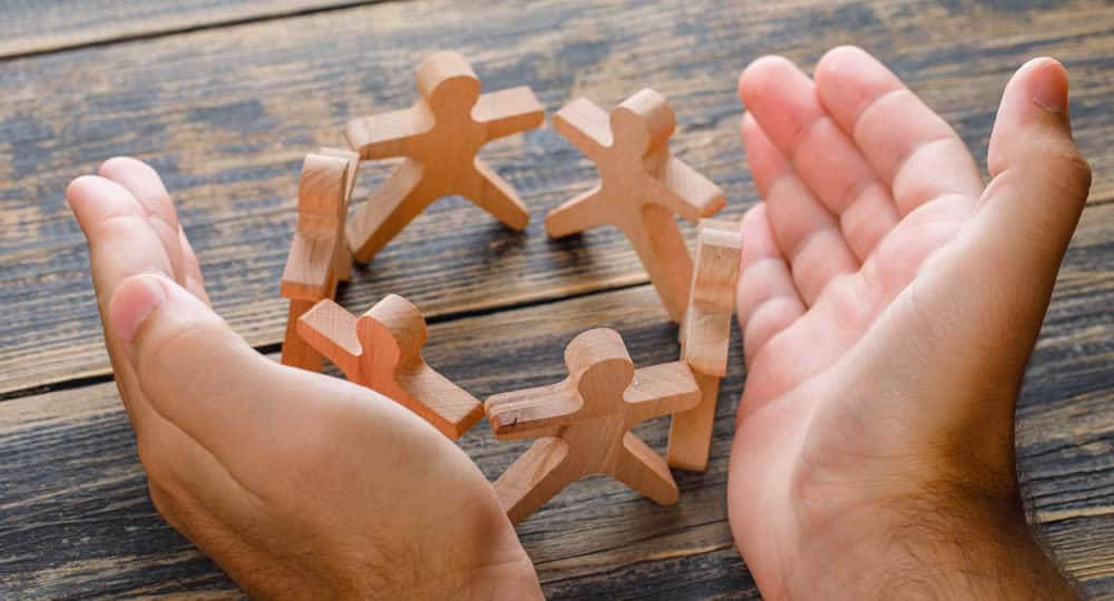 Duas mãos organizando um conjunto de bonecos de madeira sobre uma mesa, representando o conceito de "formação de uma equipe de RH".
